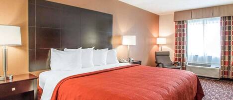 Een hotelkamer met een groot bed, twee nachtkastjes, een stoel, een raam met gordijnen en een wandradiator.