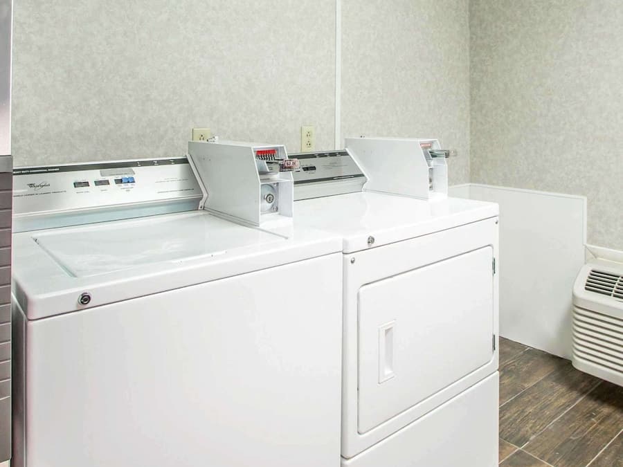 Un área de lavandería con lavadora y secadora de carga frontal, un panel de control y una rejilla de ventilación.