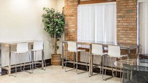 A conference room with a brick accent wall, a large potted plant, and a glass table with chairs.