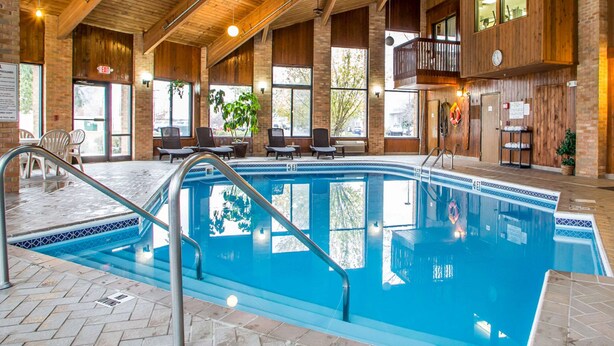 Piscina interior con techo de madera y paredes de ladrillo, rodeada de sillones de descanso y vistas al exterior.