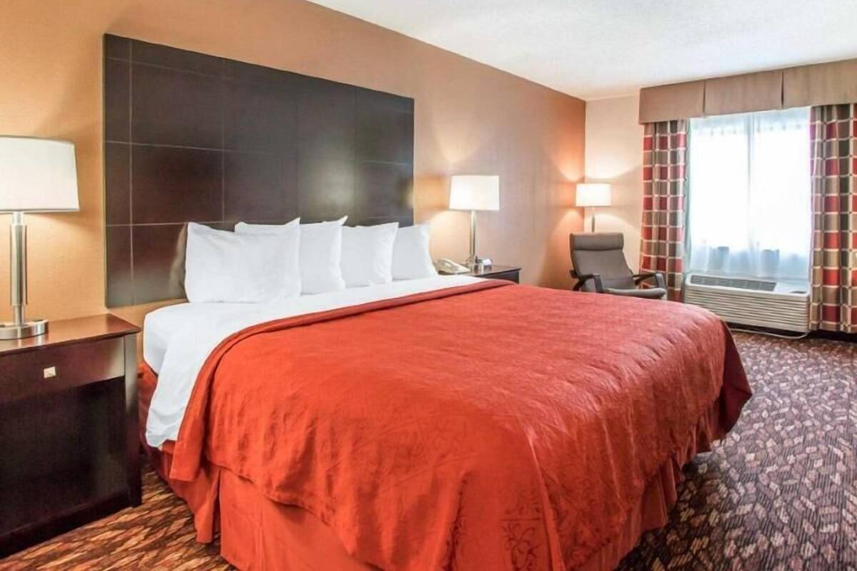 A hotel room with a large bed, two bedside tables, a chair, a window with curtains, and a wall-mounted TV.