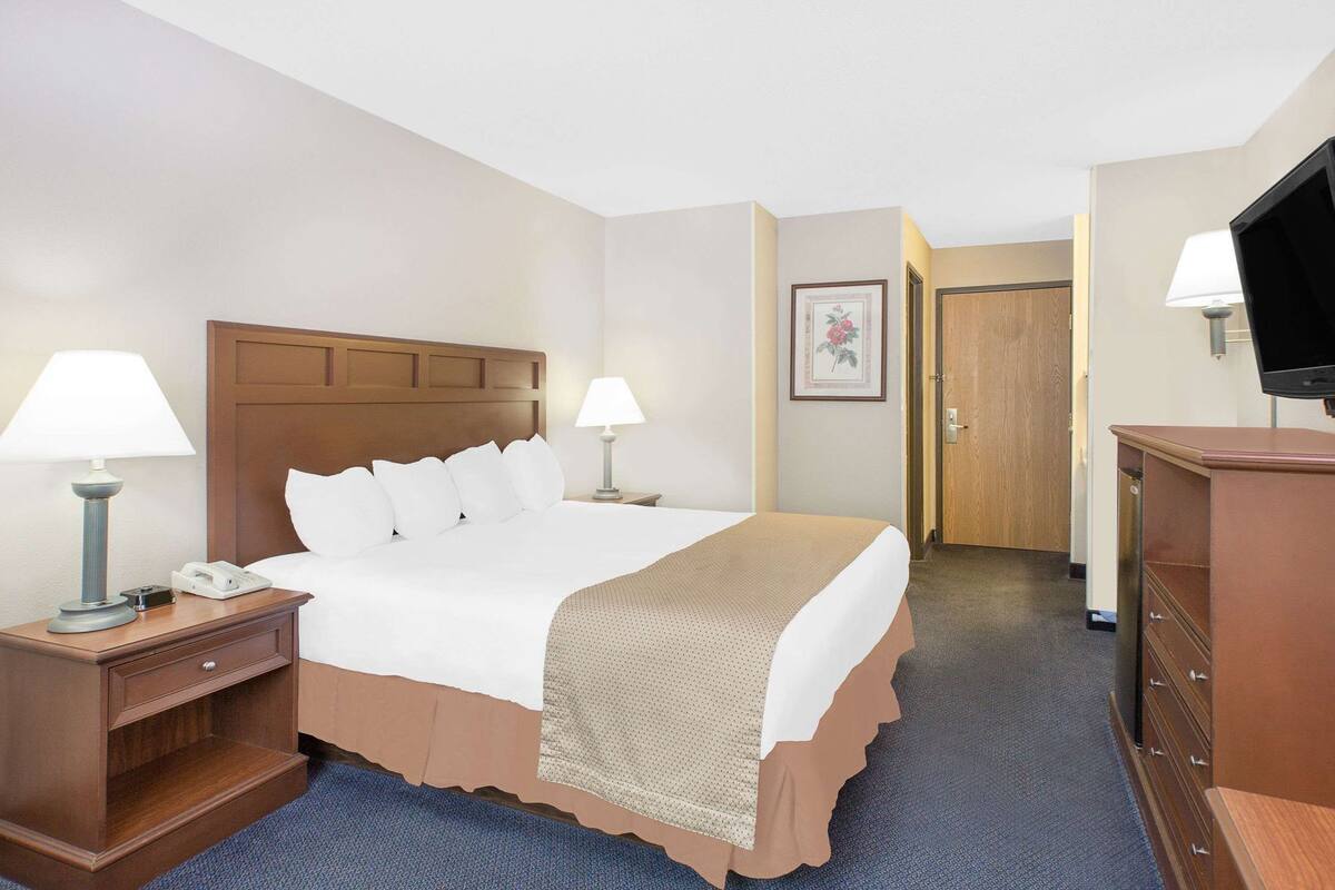 A hotel room with a bed, bedside lamps, a telephone, a dresser, a television, and a door.
