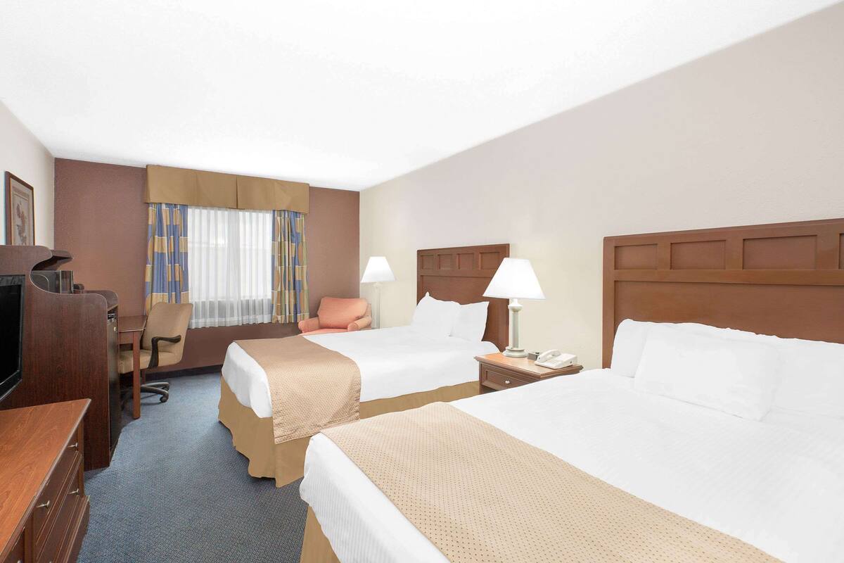 A hotel room with two beds, a desk, a chair, a TV, and a window with curtains.