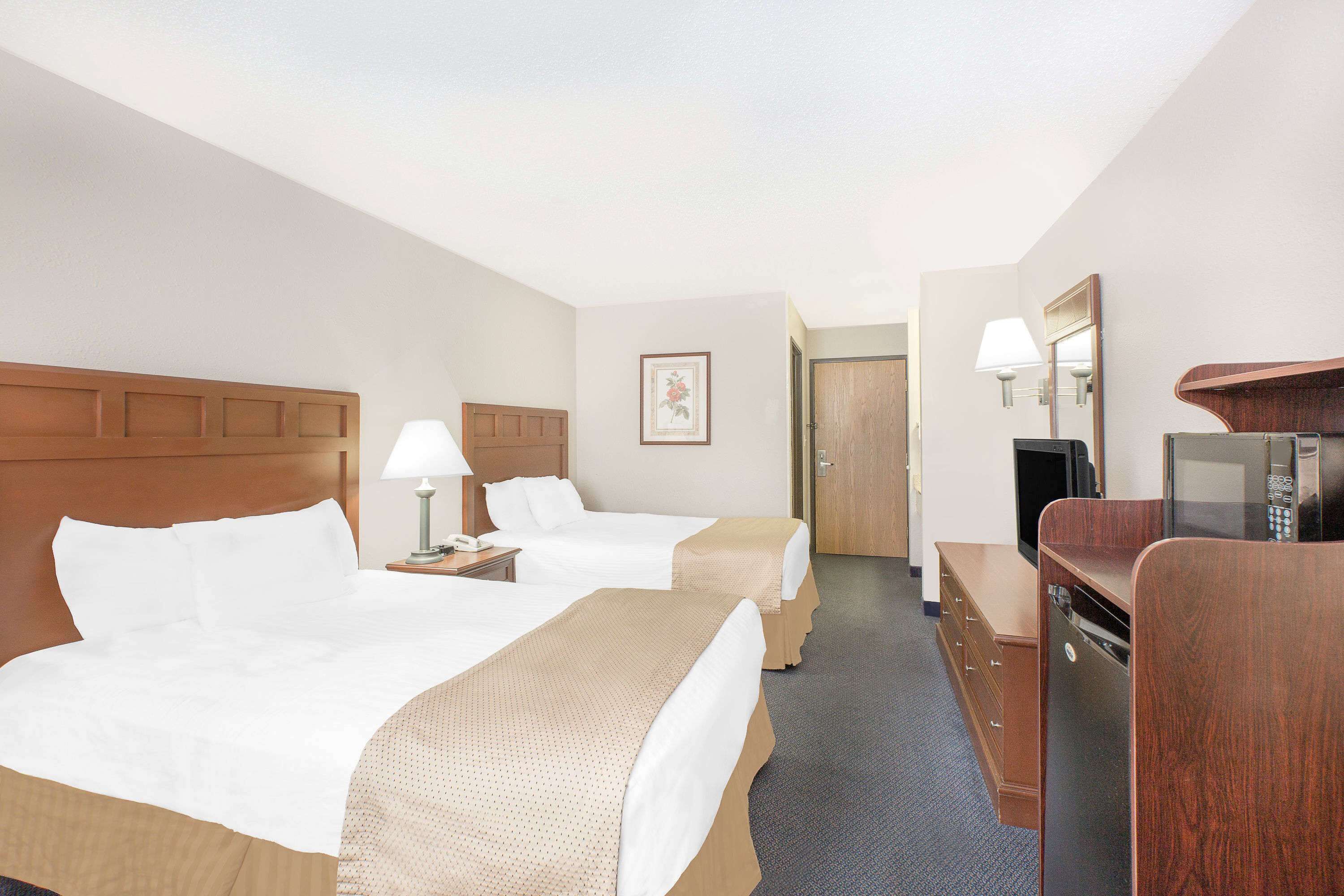 A hotel room with two beds, a desk with a television, a mirror, and a dresser.