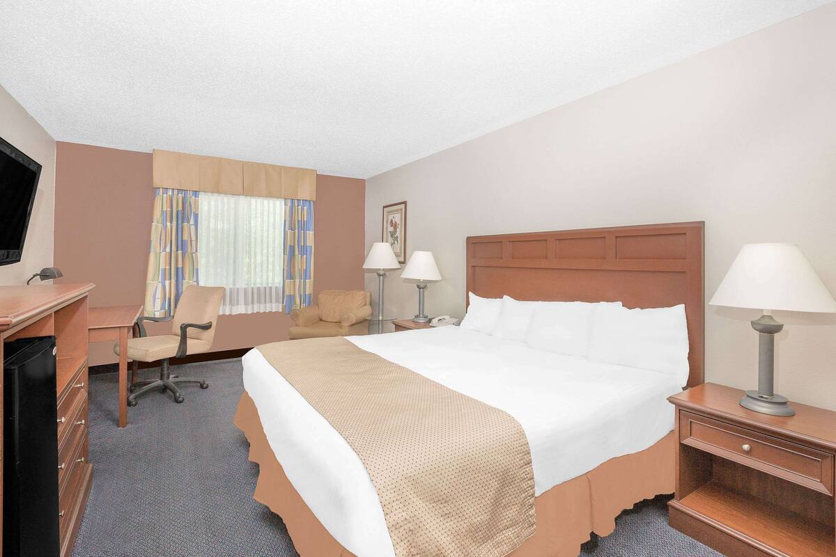 A hotel room with a bed, desk, chair, and two bedside lamps.
