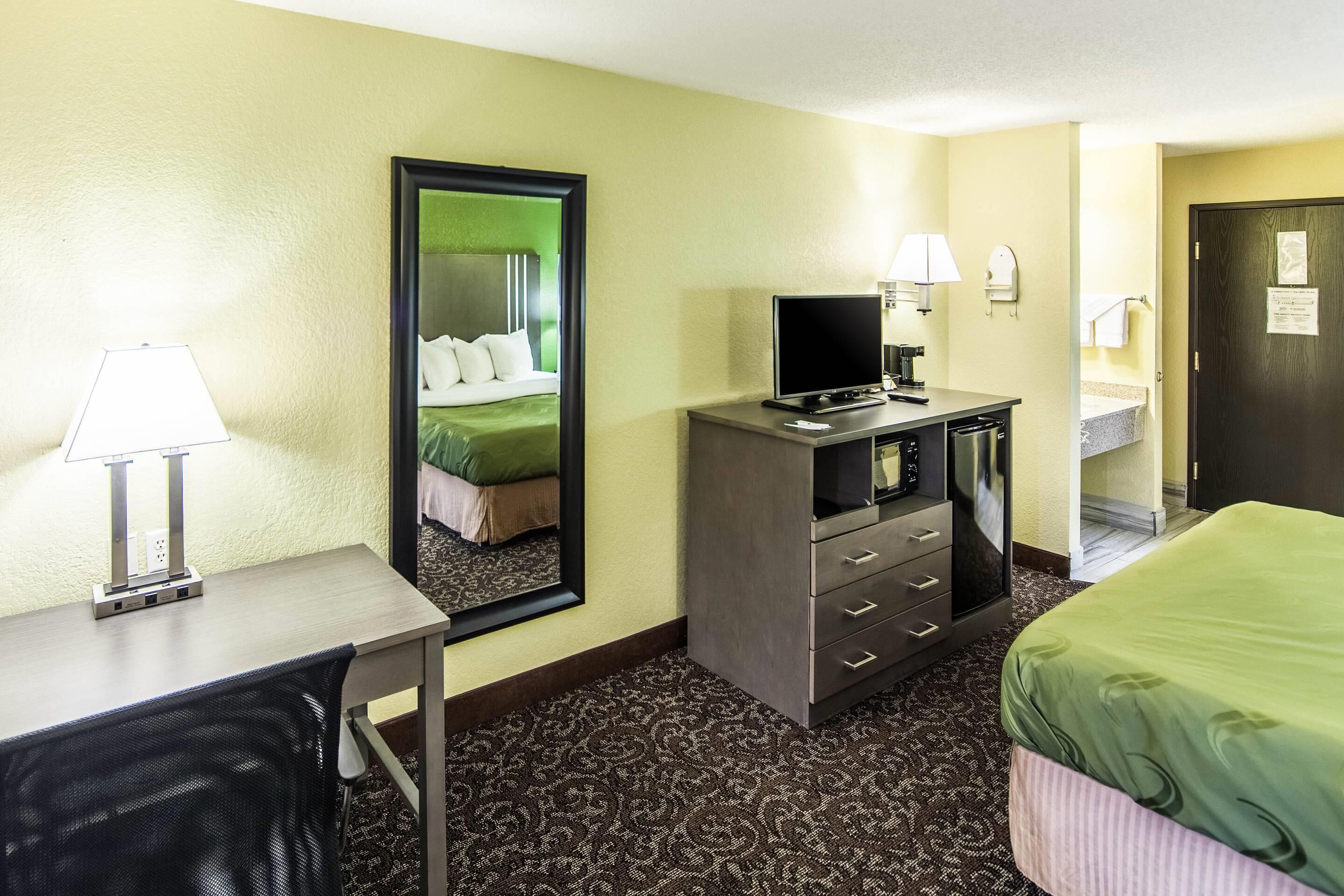 Een hotelkamer met een bed, een bureau met een lamp, een televisie, een dressoir en een spiegel.