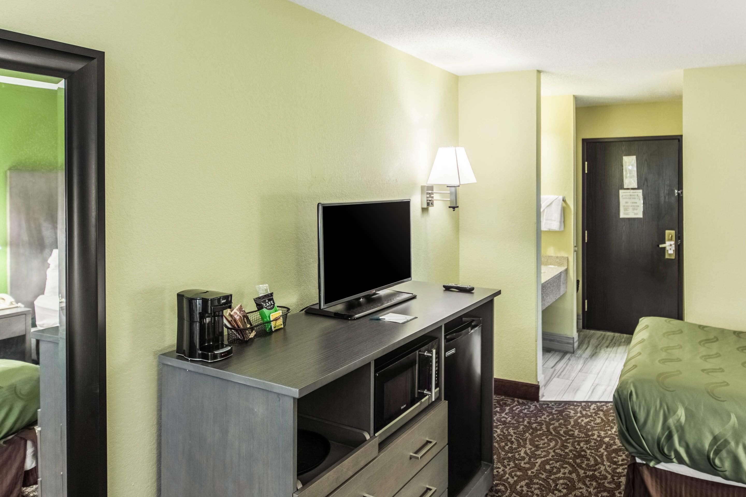 A hotel room with a bed, a desk with a television, a coffee maker, and a microwave.