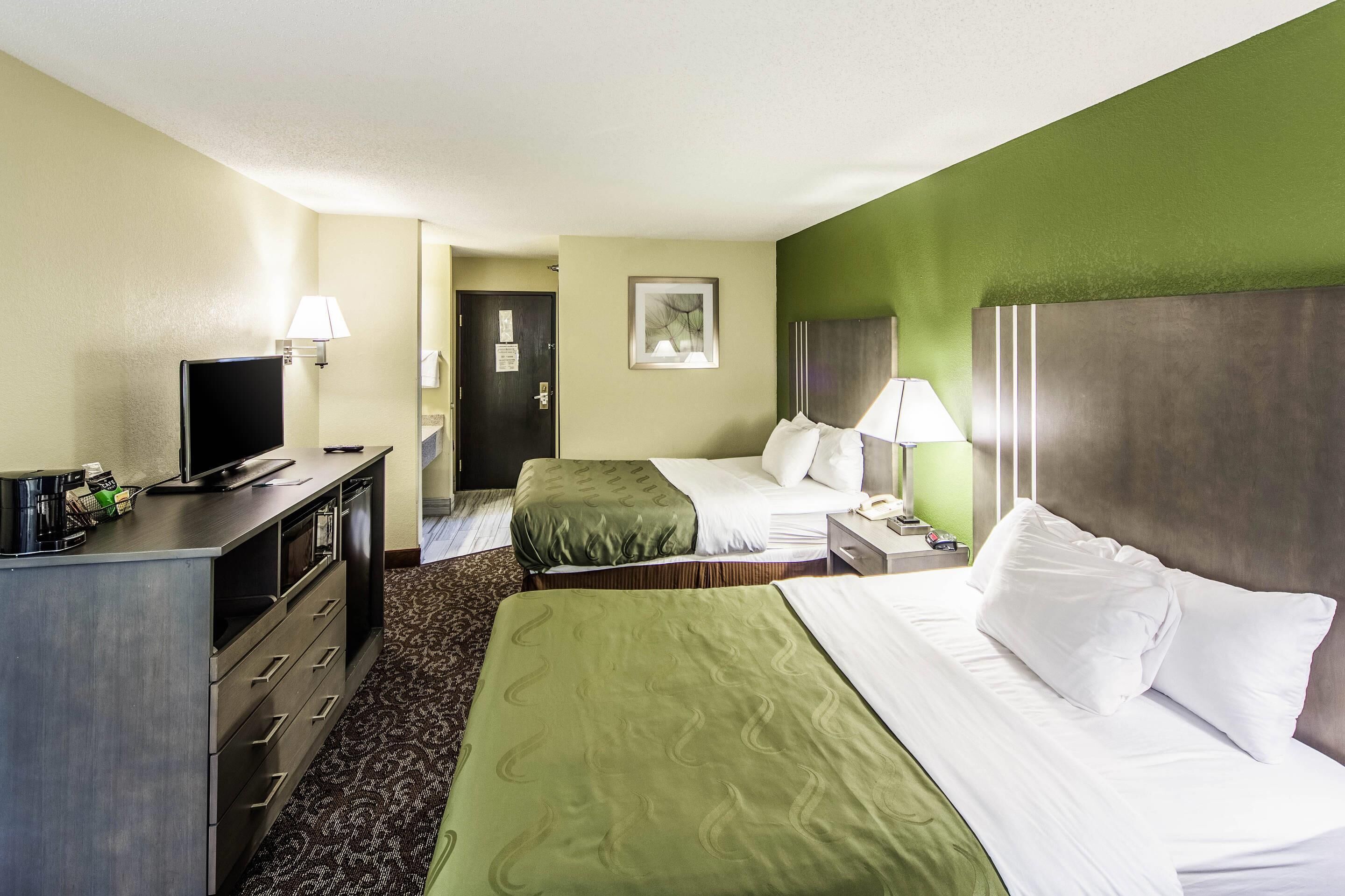 A hotel room with two beds, a desk with a TV, and a lamp.