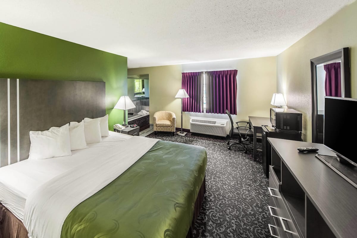 A hotel room with a large bed, a desk, a chair, a TV, and a mirror.