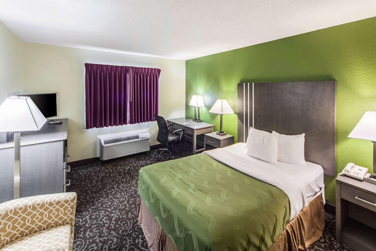Una habitación de hotel con cama, escritorio, silla y televisor.
