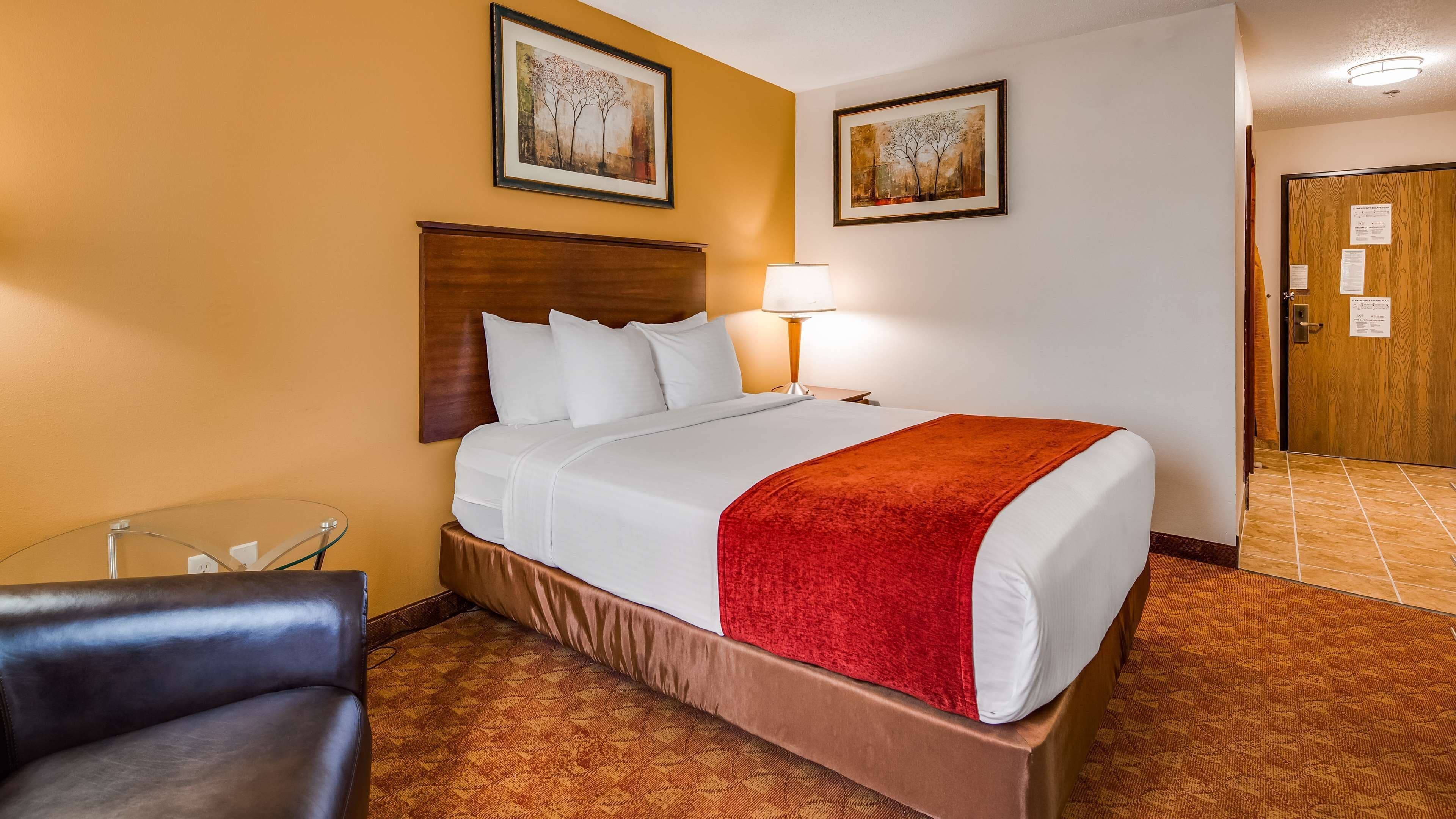 A hotel room with a bed, a chair, a lamp, and two framed pictures on the wall.