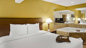 Habitación de hotel con una cama grande, una mesita de noche con lámpara, un baño con bañera y un espejo que refleja la habitación.