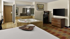 Una habitación de hotel con una cama grande, una bañera, un televisor, un microondas y un escritorio con una silla.