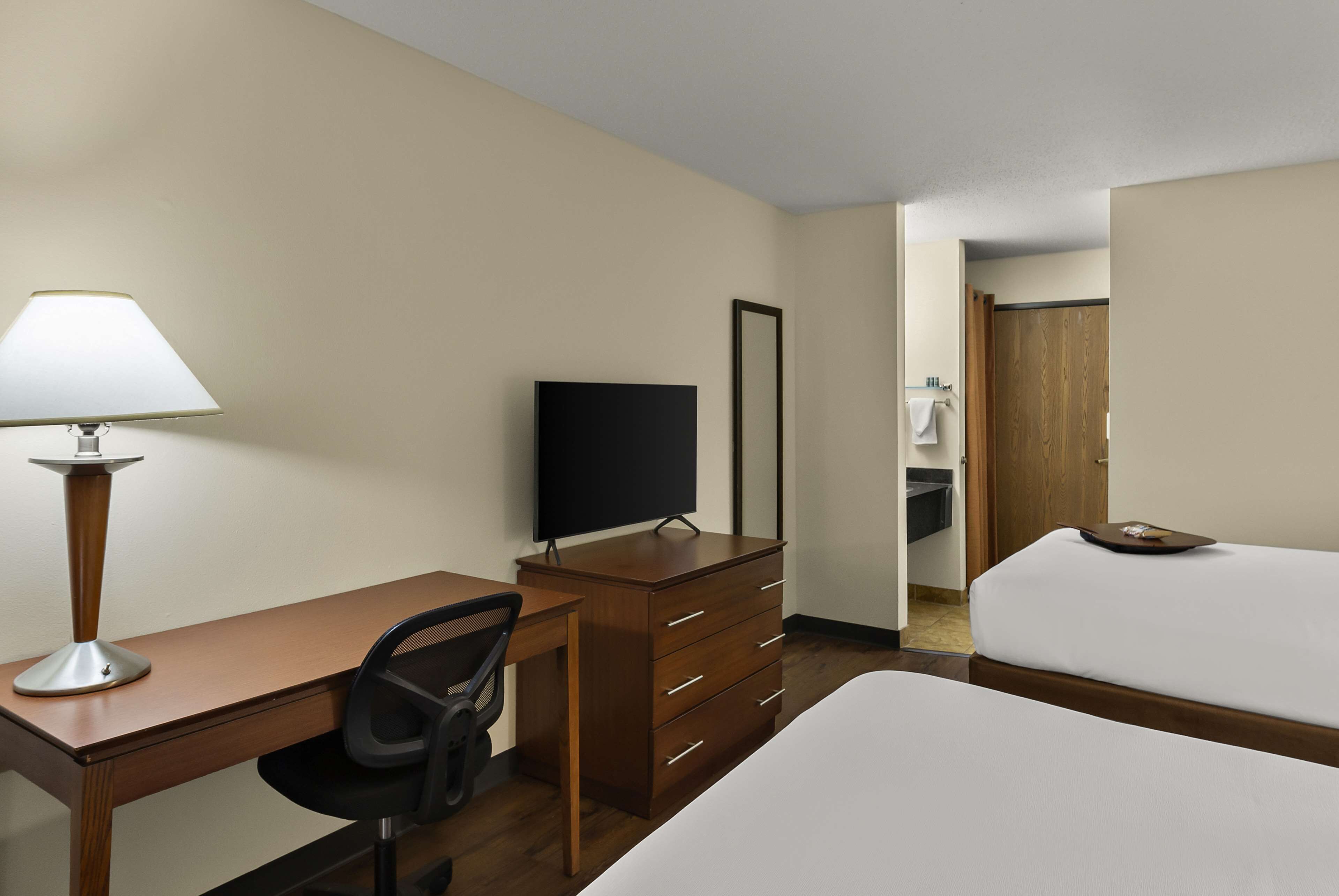 A hotel room with a desk, chair, TV, dresser, and a bed.