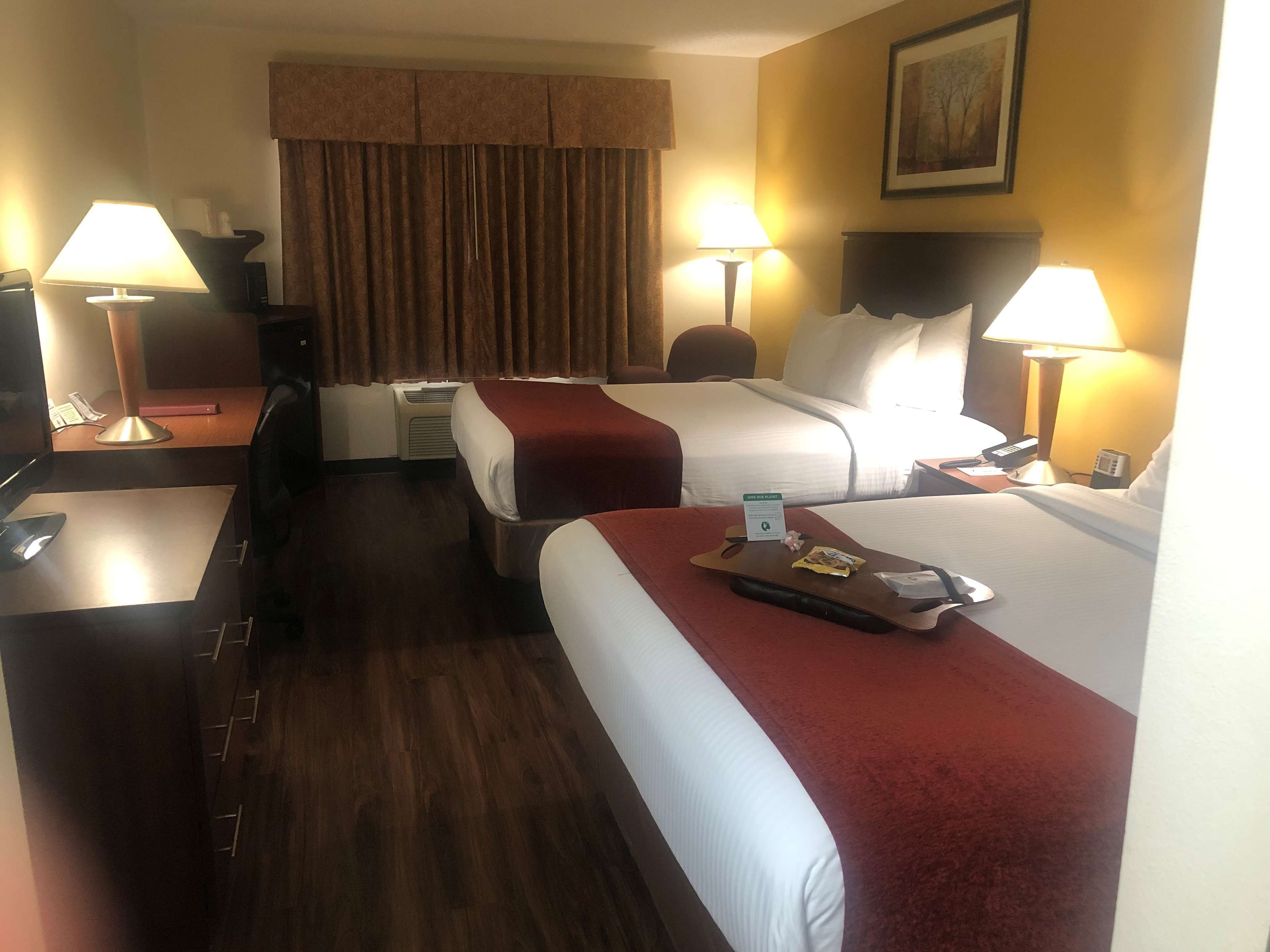 A hotel room with two beds, a desk, a chair, a lamp, a telephone, and a painting on the wall.
