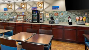 Restaurante de hotel con mostrador, zona de asientos y diversas opciones de comida y bebida.