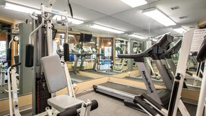 Un gimnasio con máquinas de cardio, pesas y un espejo grande.