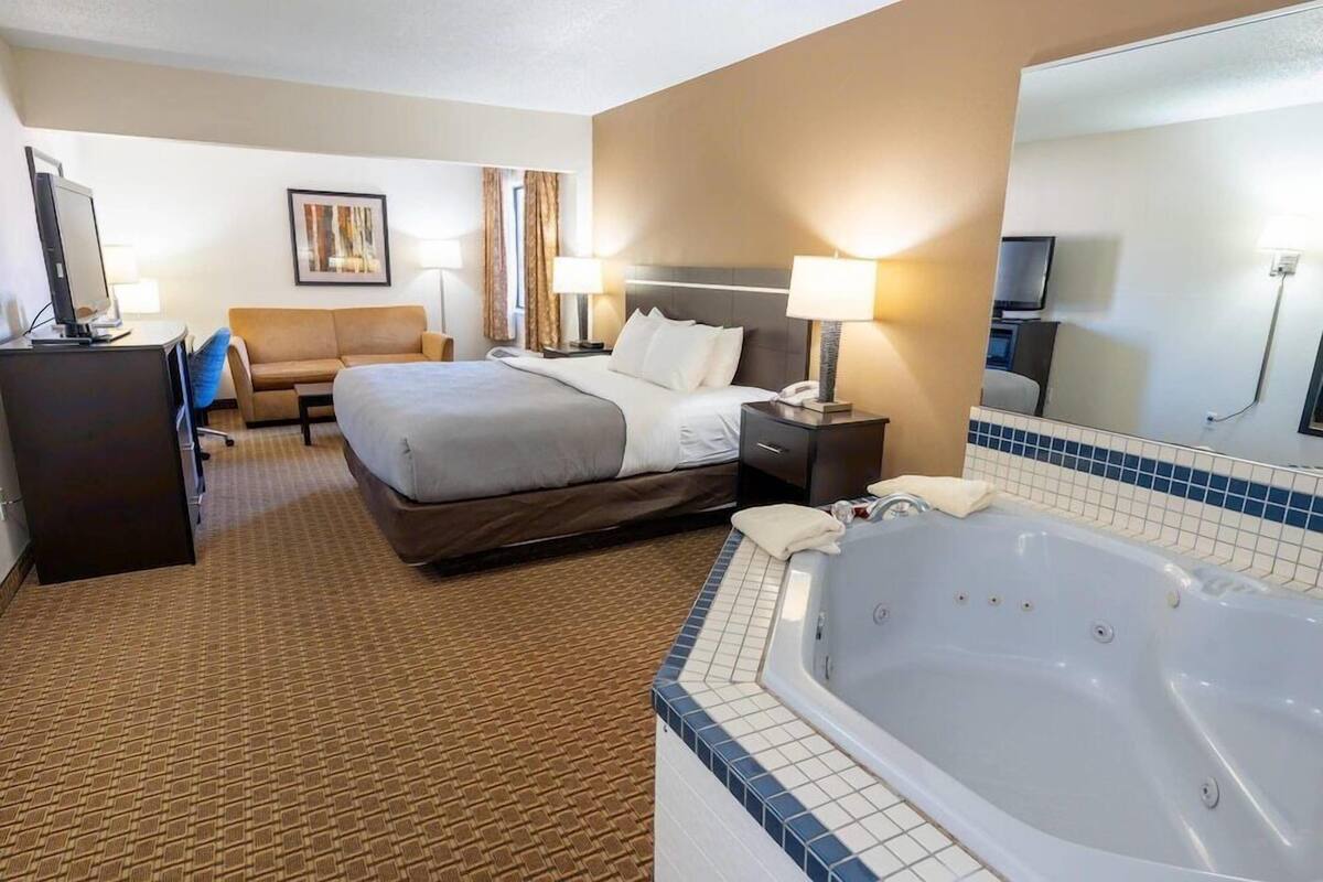 A hotel room with a bed, a desk, a chair, a sofa, a bathtub, and a television.