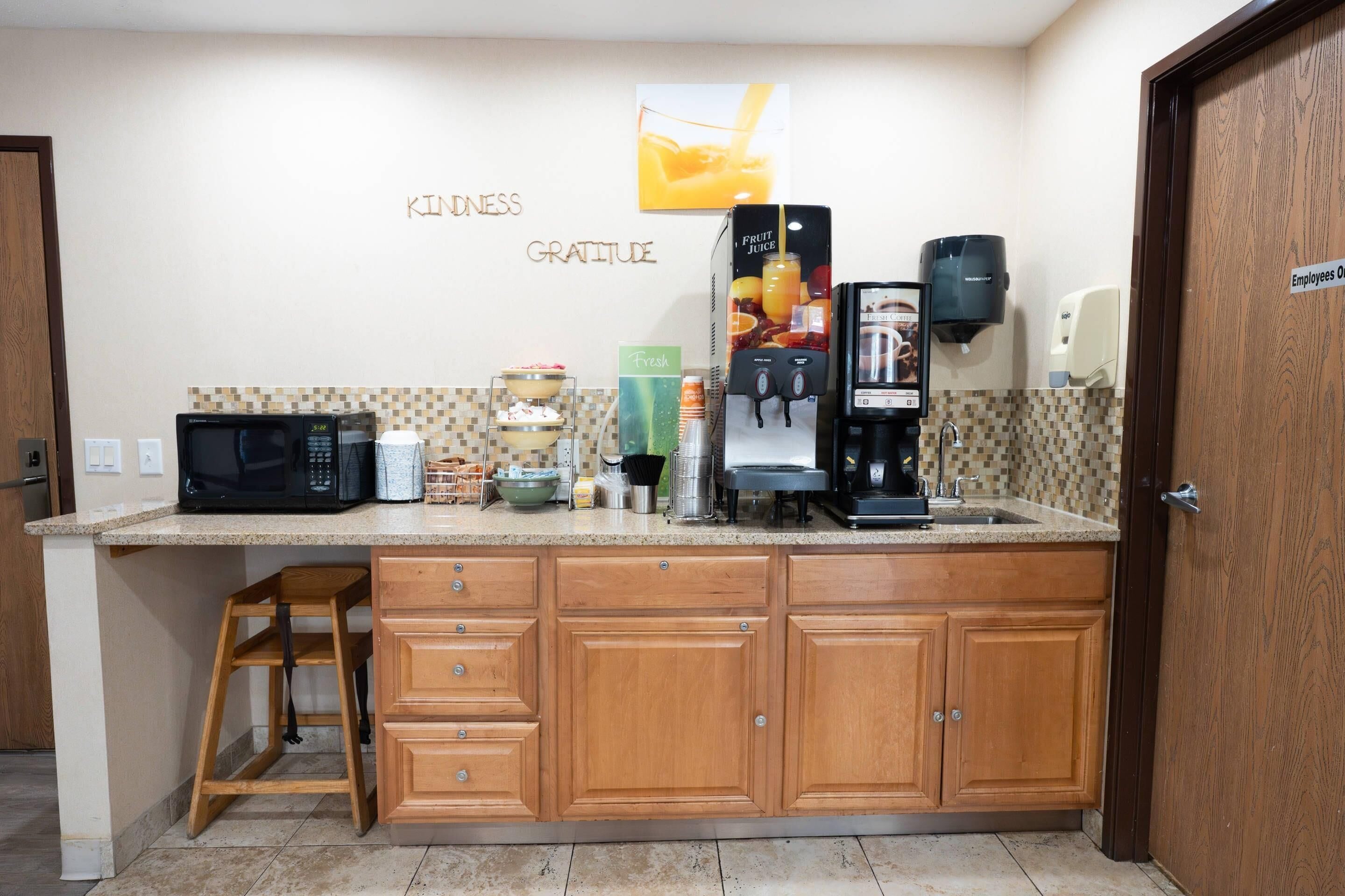 A kitchen with a microwave, coffee maker, and fruit juice dispenser.