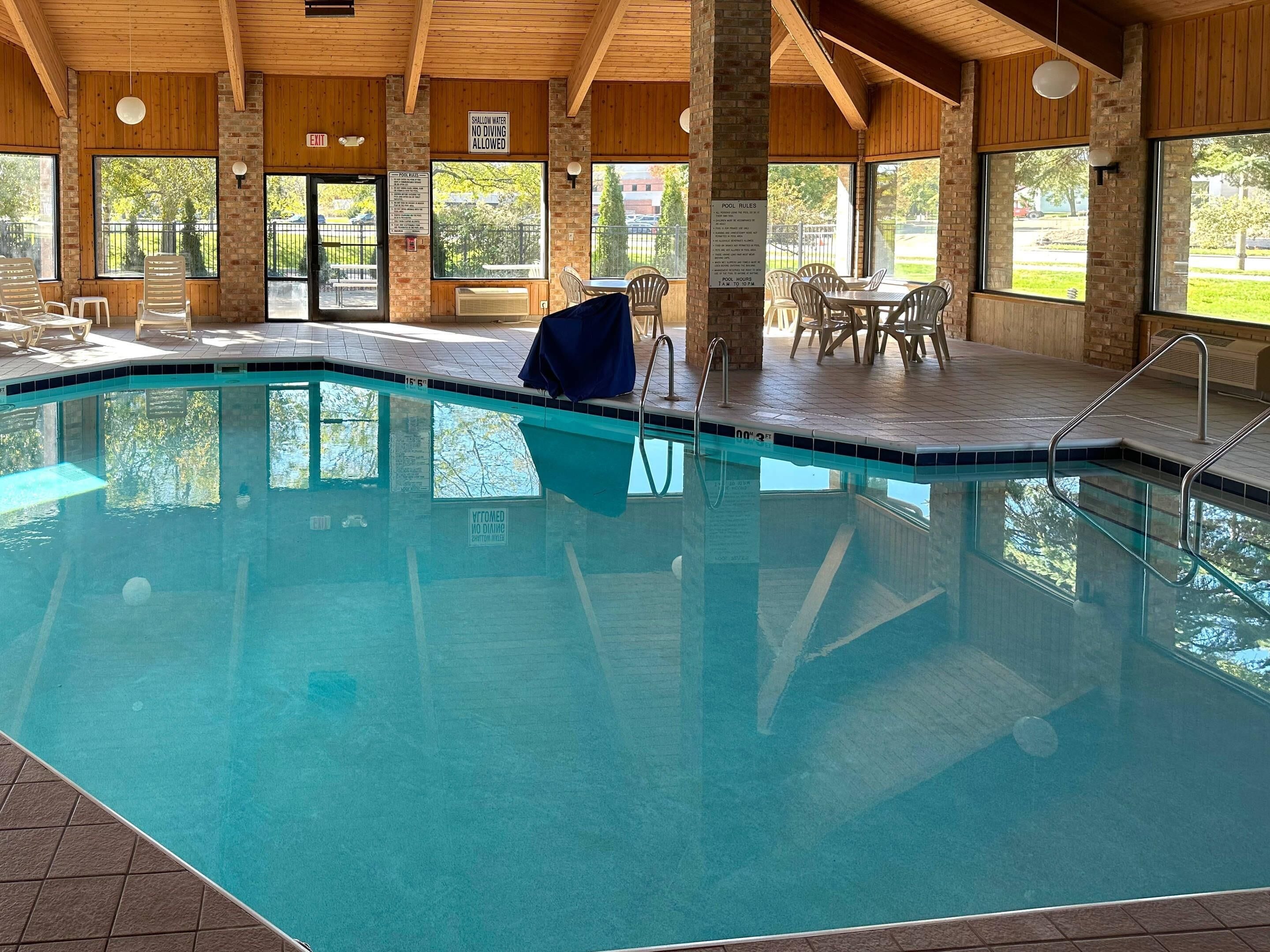 An indoor swimming pool with clear pool rules and shallow water signage, surrounded by wooden walls and large windows.