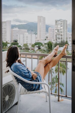 A person seated on a balcony chair with a cityscape and water in the background. - Coconut Waikiki Hotel (Honolulu)