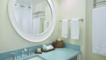 A bathroom with a round mirror, a sink with two faucets, and a towel rack with several white towels.