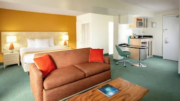 A hotel room with a bed, a brown sofa, a desk with a chair, and a kitchenette.
