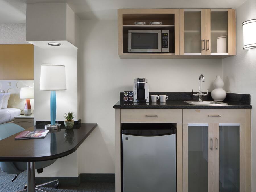 Een kleine hotelkamer met een kitchenette, een bed, een bureau en een lamp.