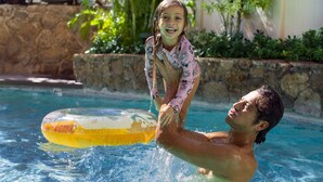 A man and a child in a swimming pool with a stone wall and greenery in the background. - Coconut Waikiki Hotel (Honolulu)