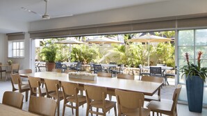 A spacious indoor dining area with large windows, wooden tables and chairs, and potted plants. - Coconut Waikiki Hotel (Honolulu)