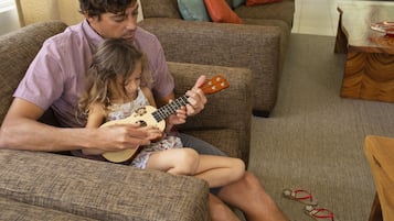 A man and a child sitting on a couch playing a ukulele.