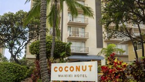 A sign for the Coconut Waikiki Hotel with a view of the building and surrounding greenery. - Coconut Waikiki Hotel (Honolulu)
