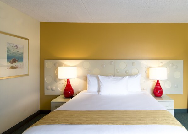 A hotel room with a bed, two bedside tables, two red lamps, a white headboard with circular patterns, and a framed picture on the wall. - Coconut Waikiki Hotel (Honolulu)