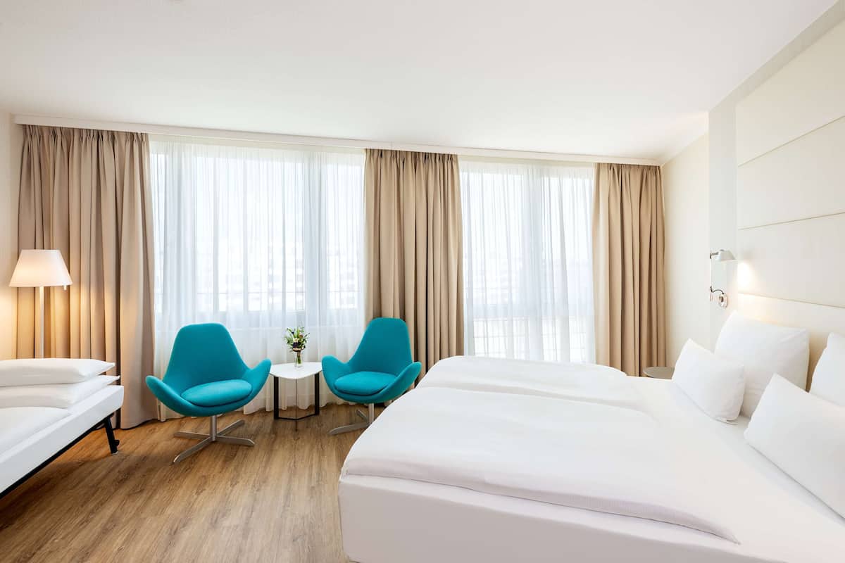 Ein Hotelzimmer mit einem großen Bett, zwei blauen Stühlen, einem kleinen Tisch und einer Lampe.