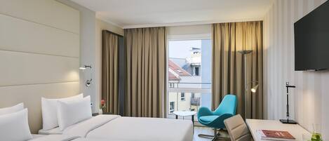 Quarto de hotel com duas camas, uma mesa, uma cadeira, televisão e vista para edifícios.