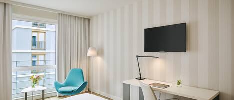 Habitación de hotel con cama, escritorio, silla, televisor y ventana con cortinas.