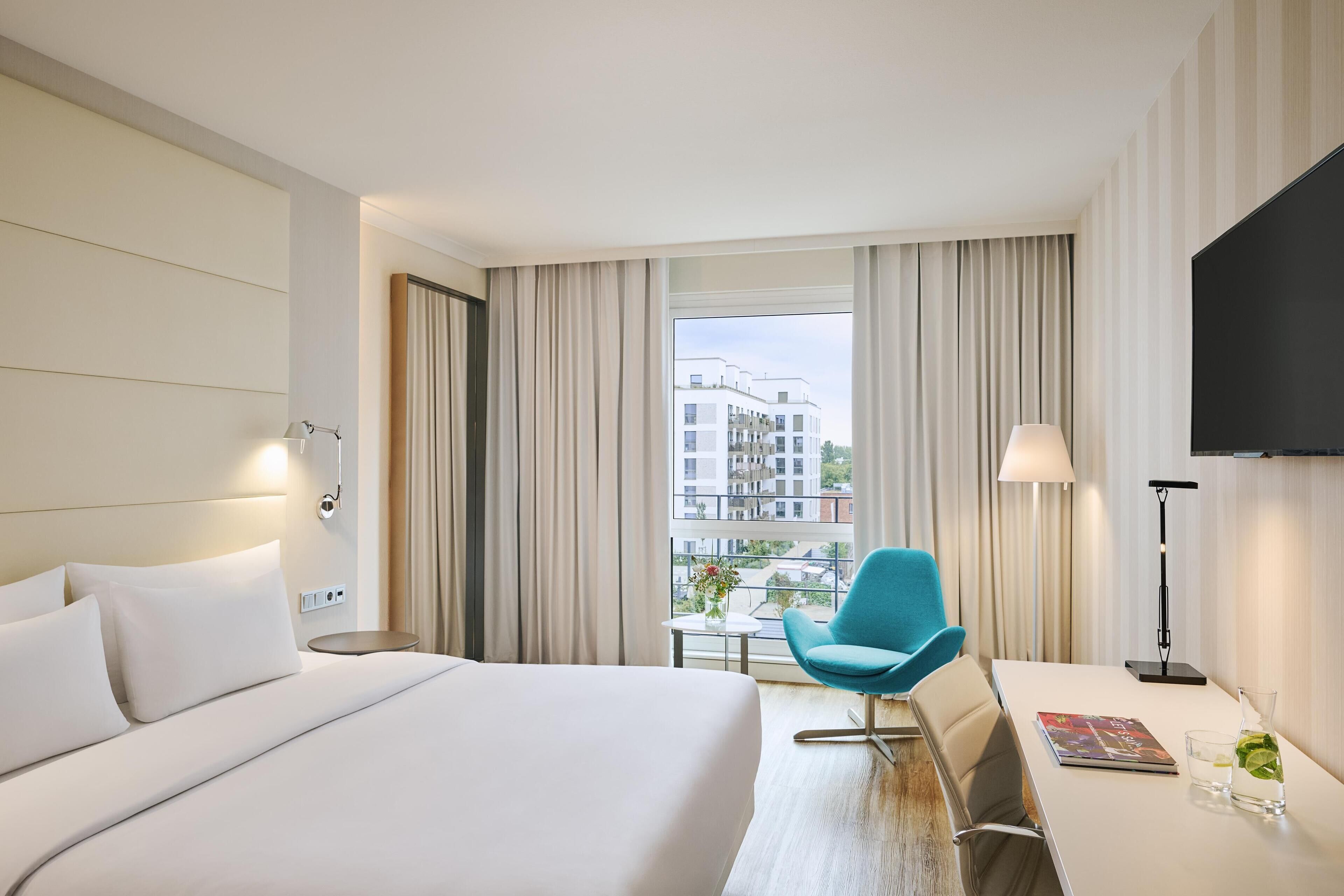 A hotel room with a large bed, a desk with a chair, a TV, and a window with curtains.