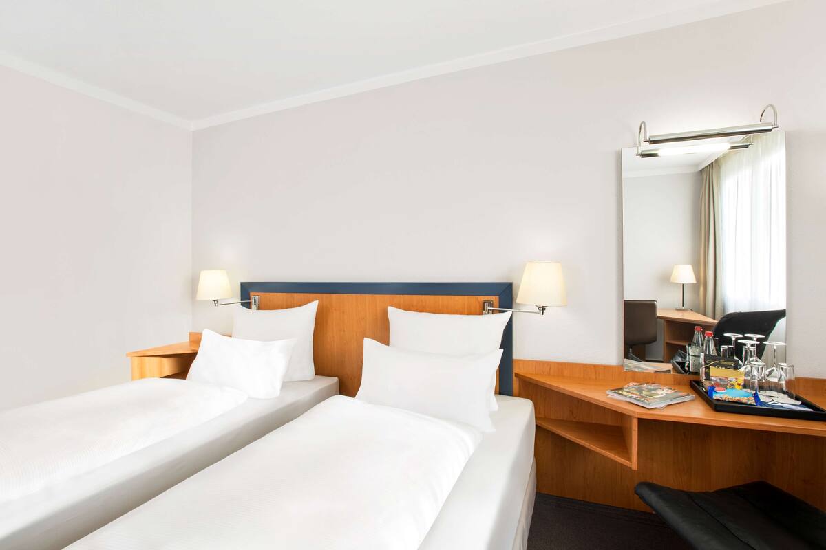 Quarto de hotel com duas camas, uma escrivaninha, uma cadeira, um espelho e um tabuleiro com objetos.
