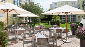 An outdoor patio with tables and chairs, umbrellas, and a well-maintained lawn. - NH Frankfurt Airport West (Raunheim)