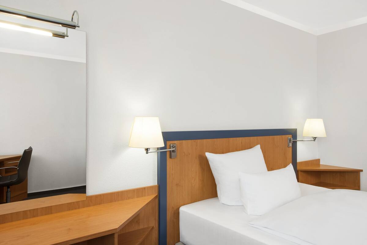 Une chambre d’hôtel comprenant un lit, deux tables de chevet avec des lampes, un bureau avec une chaise et un banc en bois.