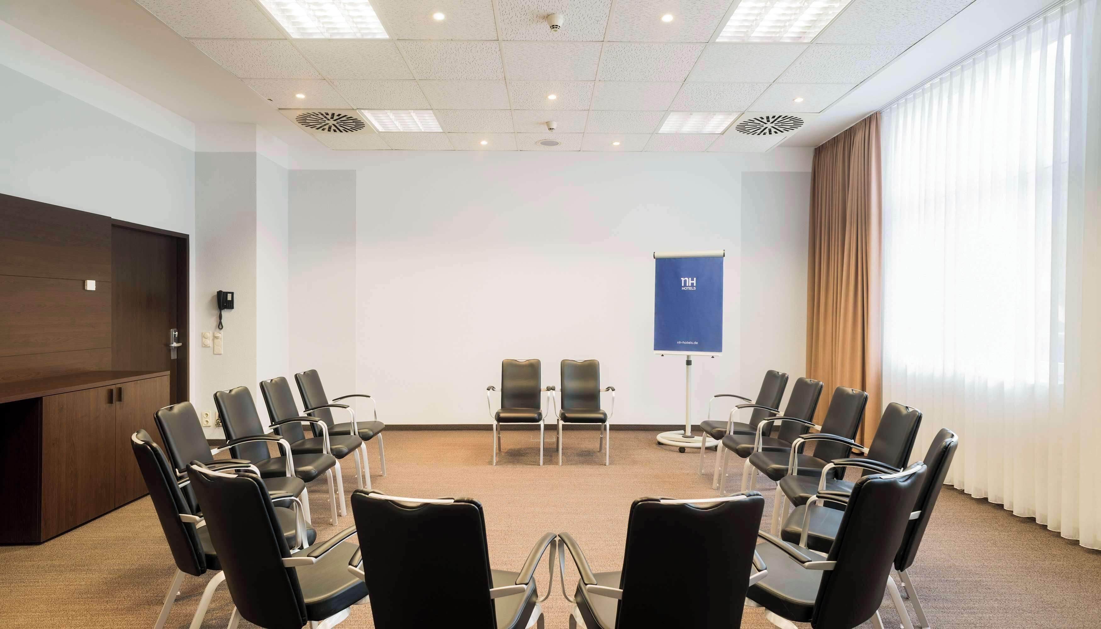 A conference room with a large table, multiple chairs, a projector screen, and a window with curtains.