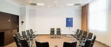 A conference room with a large table, multiple chairs, a projector screen, and a window with curtains.