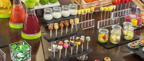 Variedad de alimentos y bebidas presentados en una mesa, incluyendo frutas, jugos y postres.