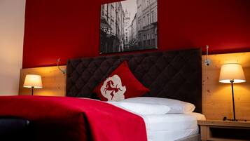 Ein Hotelzimmer mit roter Wand, einem Bett mit weißer Bettwäsche, einem rot-weißen Kopfkissen, zwei Nachttischlampen und einem schwarzen und weißen Foto im Rahmen über dem Bett.