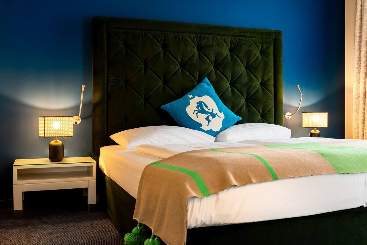 A neatly made bed with a green headboard, white pillows, and a blue pillow with a dragon design. There are two bedside lamps on white nightstands.