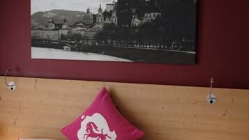 Un lit bien fait, avec du linge de lit blanc et un seul oreiller rose, une tête de lit en bois et un tableau représentant un bâtiment historique accroché au mur.