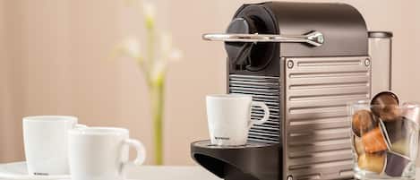 A Nespresso coffee machine with two cups and a glass of coffee on a table.