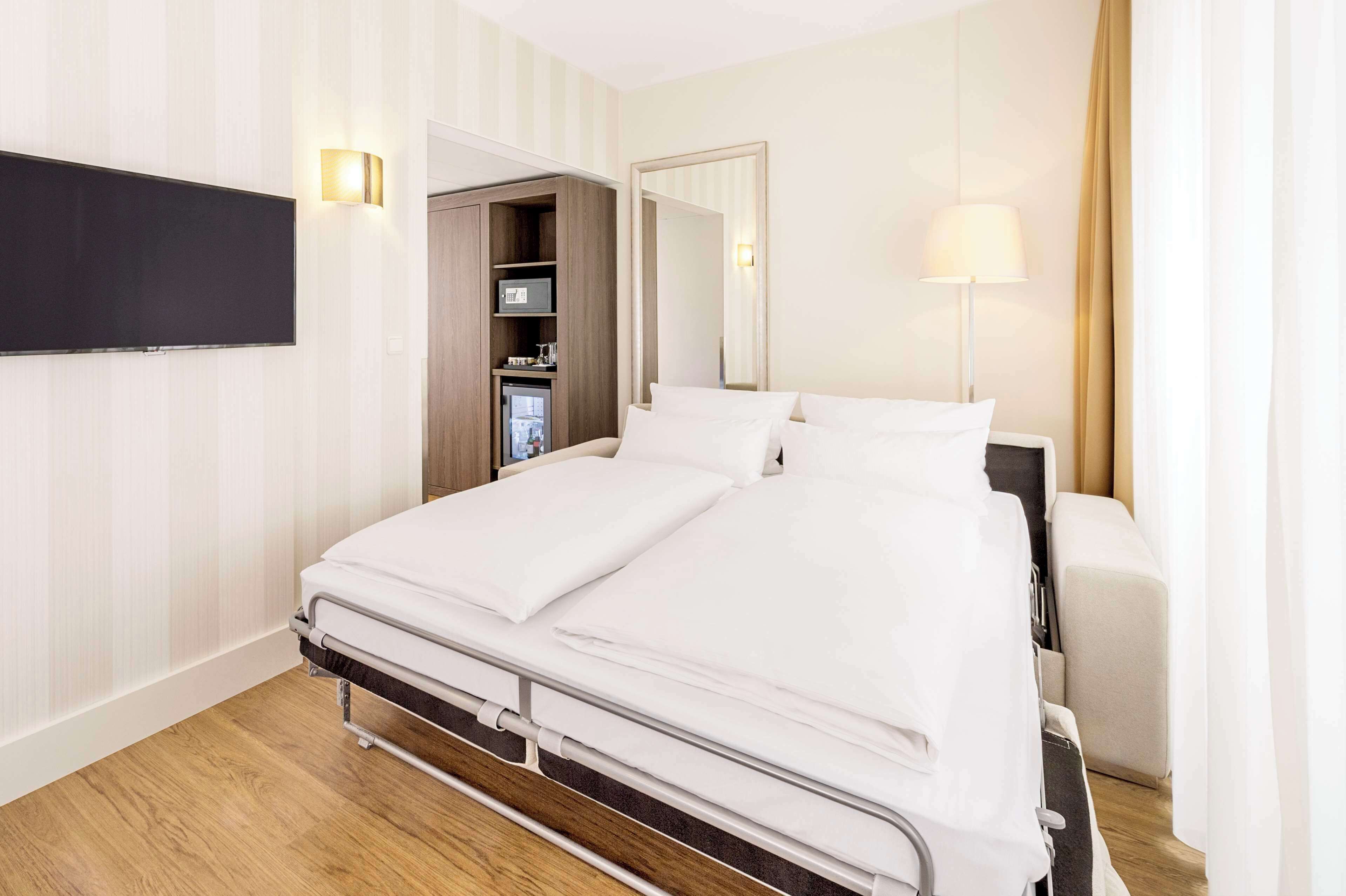 Une chambre d’hôtel avec un lit, un téléviseur fixé au mur, une lampe de chevet et une armoire.