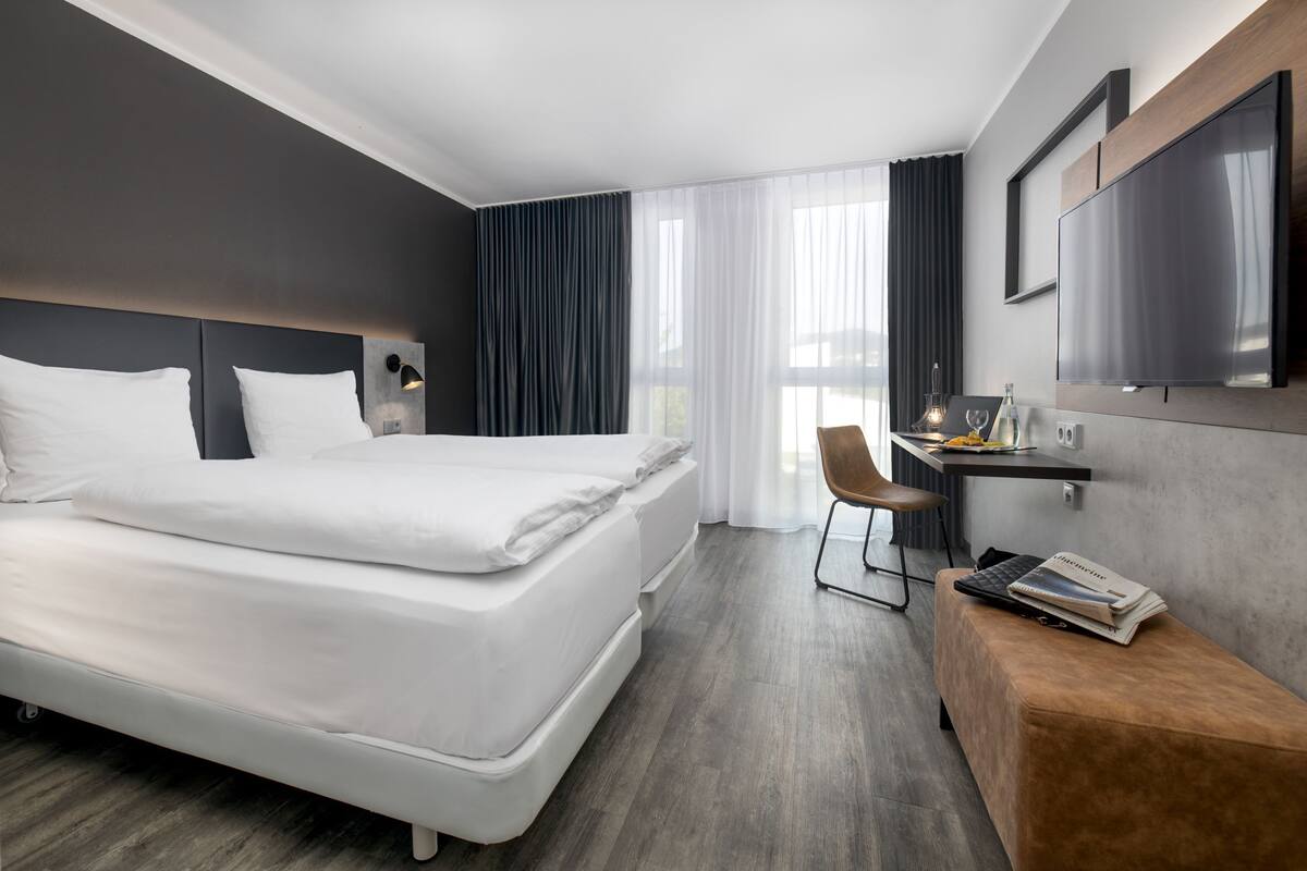 A modern hotel room with a large bed, a desk with a chair, and a flat-screen TV mounted on the wall.