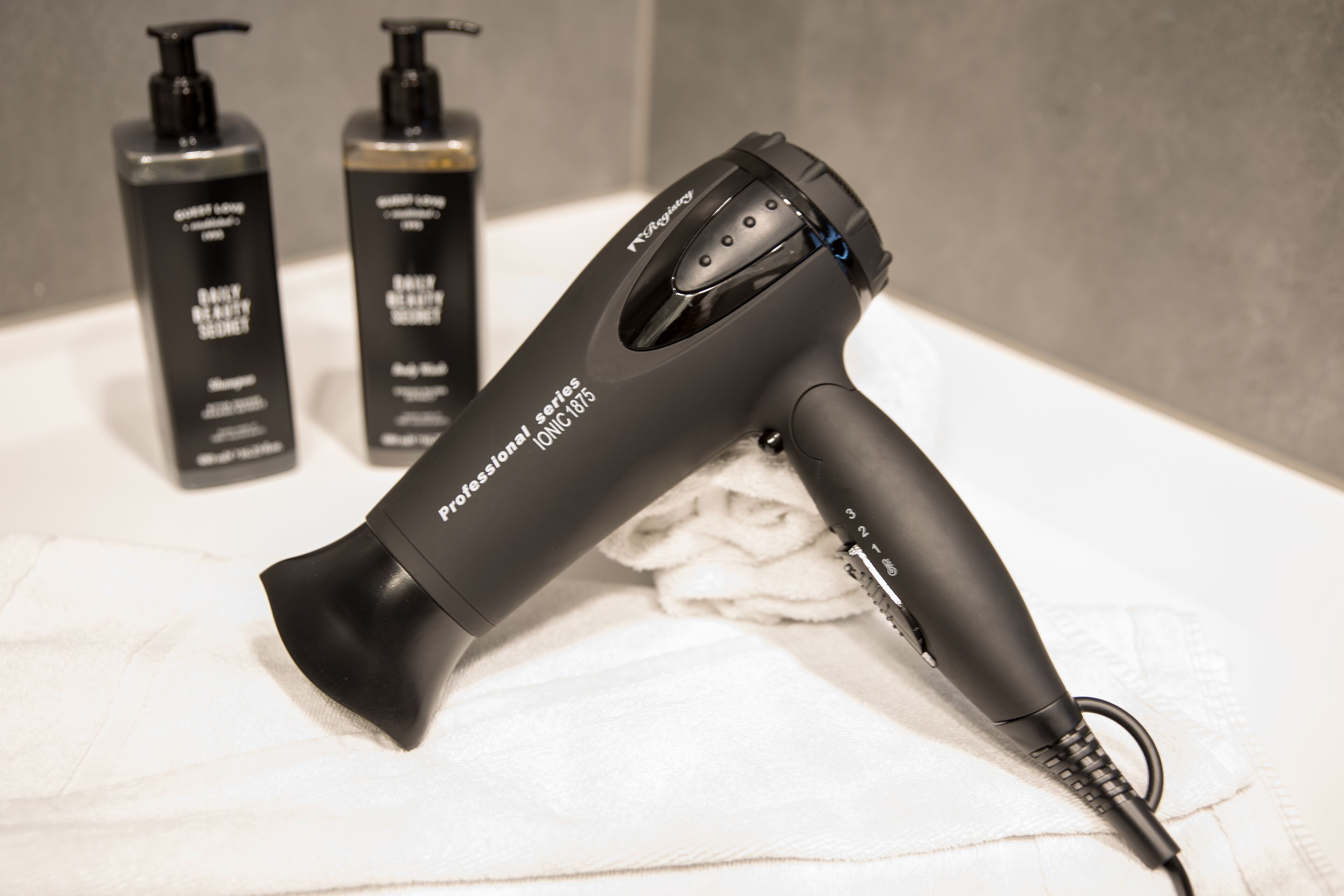 A hair dryer, two bottles of hair care products, and a towel on a bathroom counter.